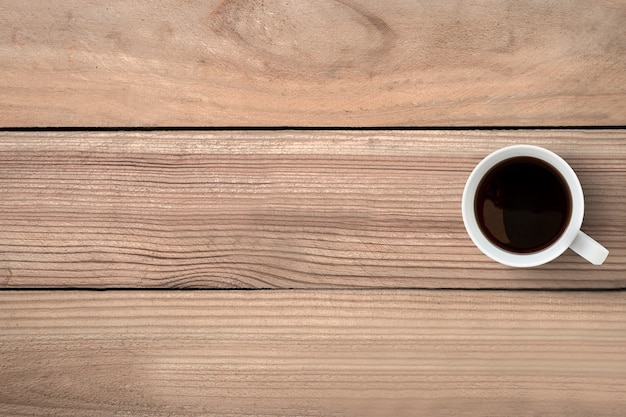 Una taza de café está encima de la mesa de madera