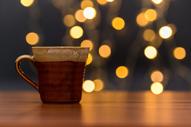 La taza de café está sobre el escritorio Fondo de luces bokeh naranja