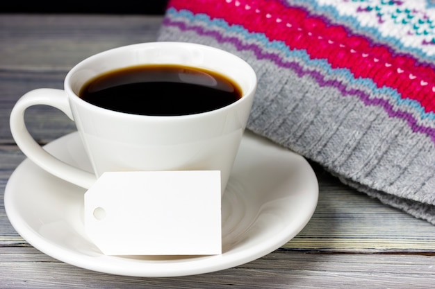 Una taza de café y una etiqueta de papel en blanco sobre una mesa de madera clara.