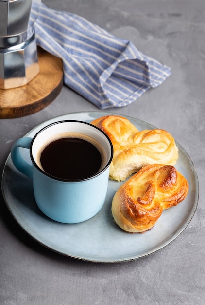 Taza de café expreso con dos bollos dulces en forma de corazón en placa sobre superficie de hormigón gris. Bodegón minimalista.