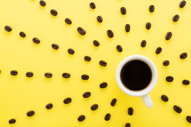 Taza de café expreso con rayos de sol de granos de café sobre fondo amarillo. Concepto de humor plano endecha, mañana soleada.