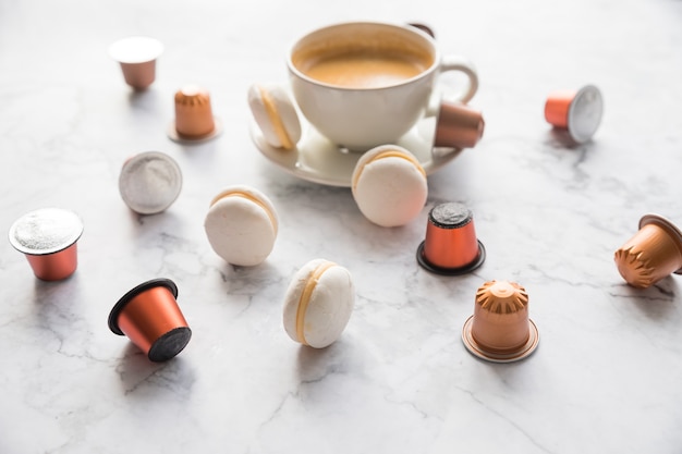 Taza de café expreso servido con macarrones y cápsulas en la mesa de mármol.