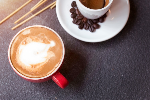 La taza del café express, el café con leche, el grano de café y las flores secas sacuden en de madera.