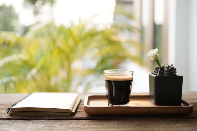 Taza de café y flor de cactus blanco en una olla negra sobre una mesa de madera con cuaderno