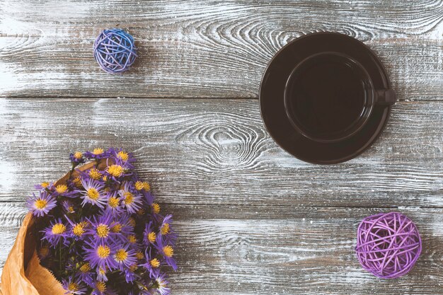 Taza de café, flor envuelta en papel kraft sobre la mesa gris desde arriba. Flat lay estilo pastel.