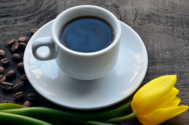 Taza de café con flor de tulipán amarillo y granos de café.