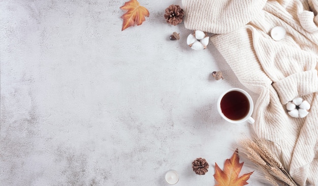 Una taza de café, flores de algodón, hojas de otoño y suéter sobre fondo de piedra