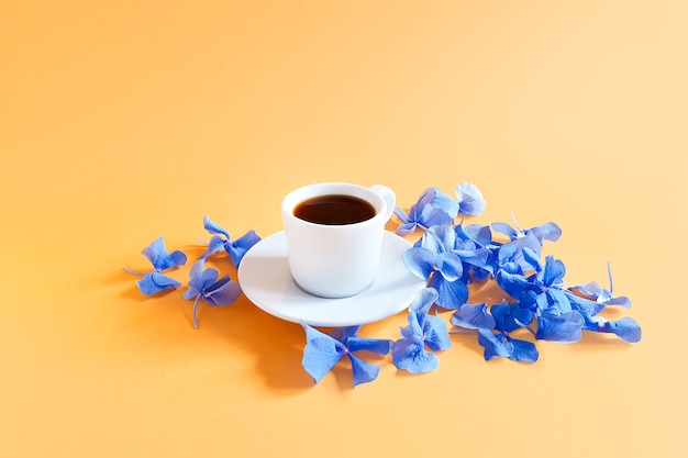 taza de café y flores de hortensia azul sobre mesa amarilla.