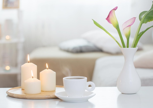 Taza de café y flores en un jarrón en el interior de la mesa blanca