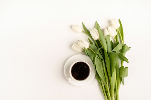 Taza de café, flores de tulipán blanco recién cortado vista superior sobre fondo blanco.