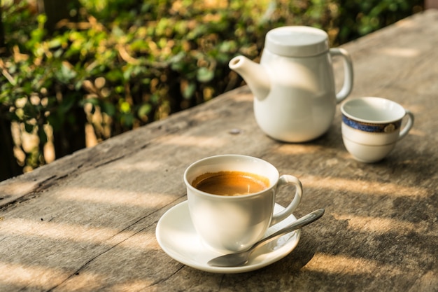 Taza de café con fondo de teteras en la mesa de madera con luz solar