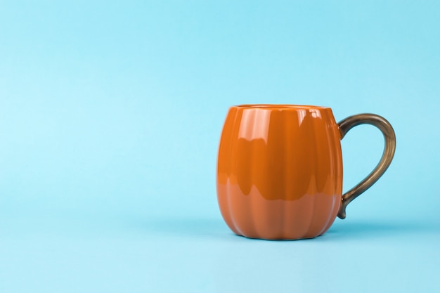 Una taza de café con forma de calabaza de color naranja brillante sobre un fondo azul. Estilo calabaza.