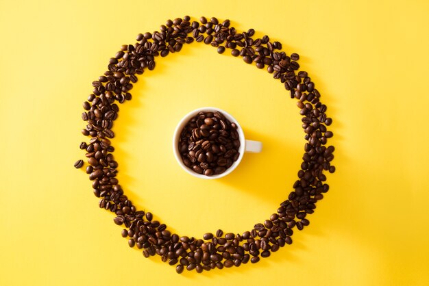 Taza de café en forma de círculo de granos de café sobre fondo amarillo