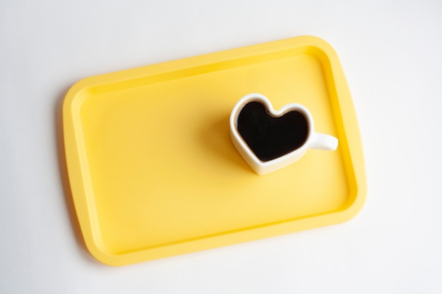 Taza de café en forma de corazón blanco en una bandeja amarilla, aislado, vista superior