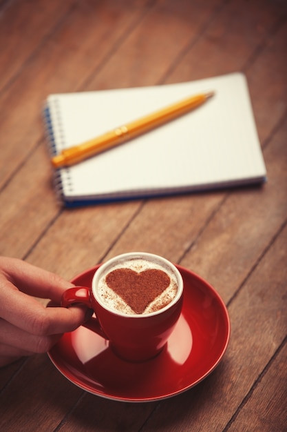 Taza de café con forma de corazón y nota con lápiz sobre una mesa de madera