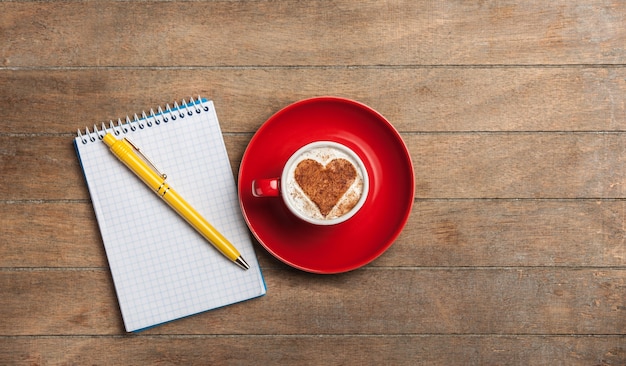 Taza de café con forma de corazón y nota con lápiz sobre una mesa de madera