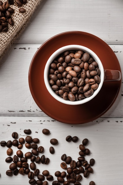 Taza de café con frijoles en el interior y granos de café sobre una mesa de madera rústica blanca