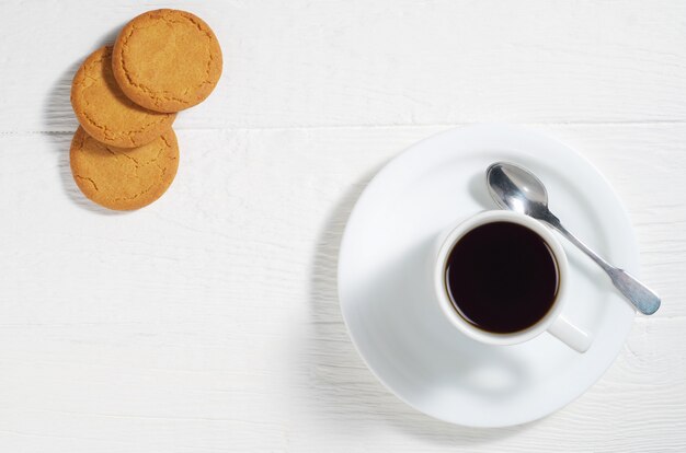 Taza de café y galletas de avena en una mesa de madera blanca