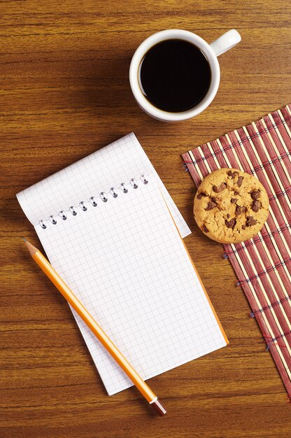 Taza de café con galletas y bloc de notas abierto