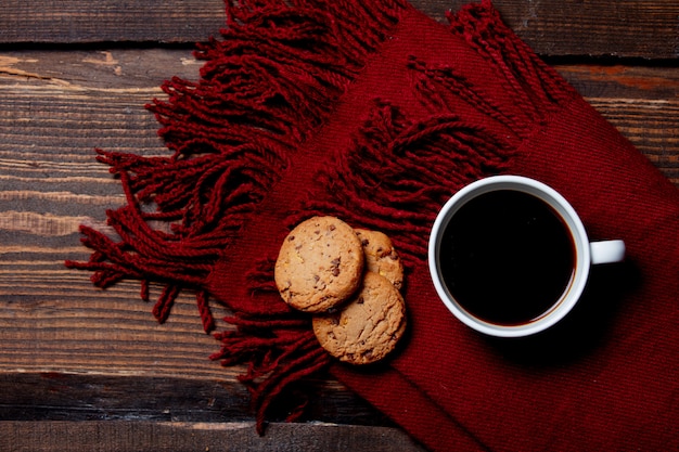 Taza de café y galletas con bufanda en mesa de madera