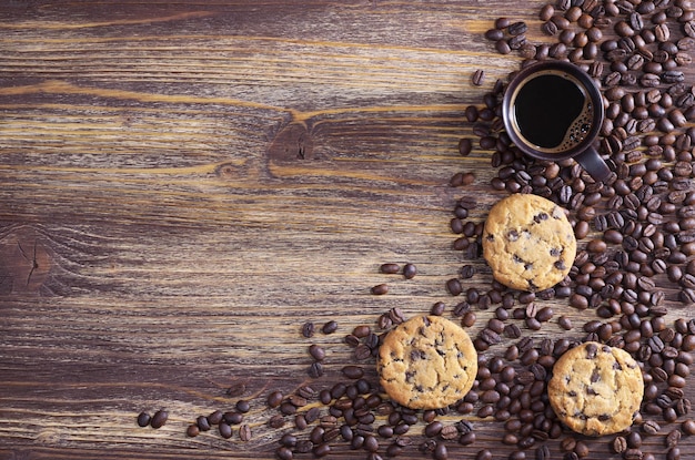 Taza de café con galletas de chocolate y frijoles dispersos sobre fondo de madera antiguo, vista superior