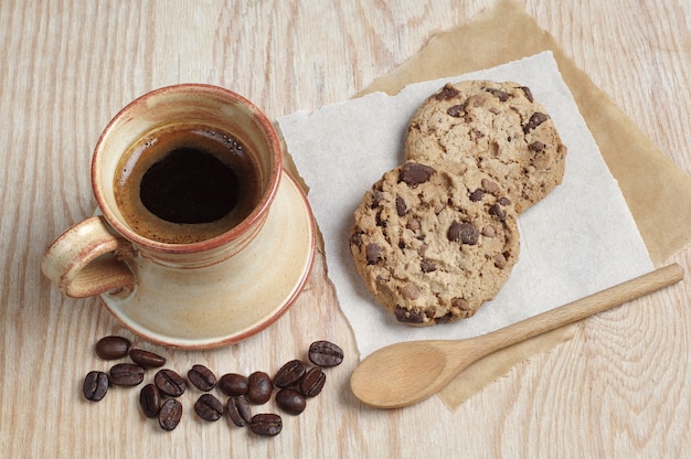 Taza de café y galletas con chocolate sobre un papel colocado sobre una mesa de madera