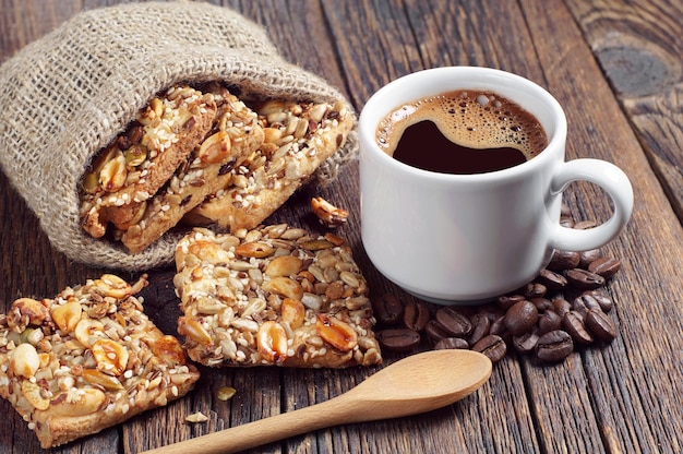 Taza de café y galletas con diferentes frutos secos en mesa de madera vintage