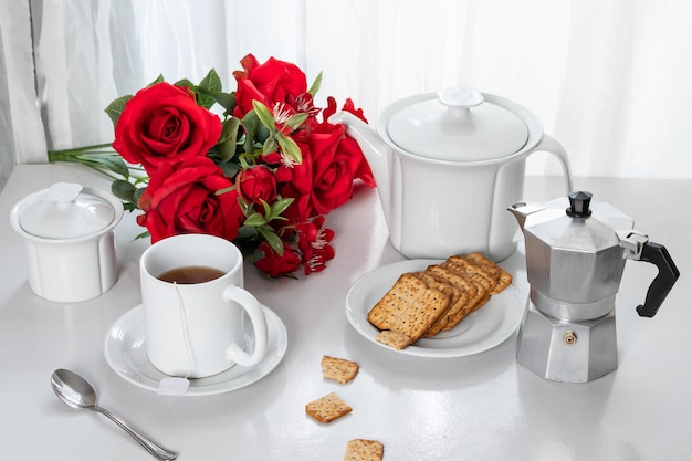 una taza de café, galletas integrales en un plato, en una mesa junto a la ventana, la luz entra por la c