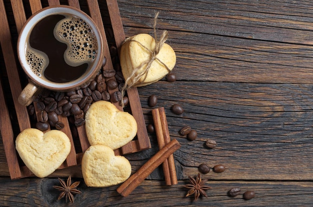 Taza de café y galletas de mantequilla en forma de corazón en la vista superior de la mesa de madera oscura con espacio para copiar