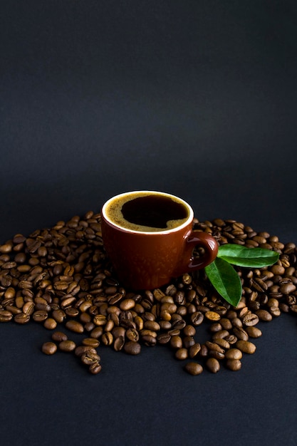 Taza de café y grano de café tostado sobre fondo negro. De cerca. Ubicación vertical.