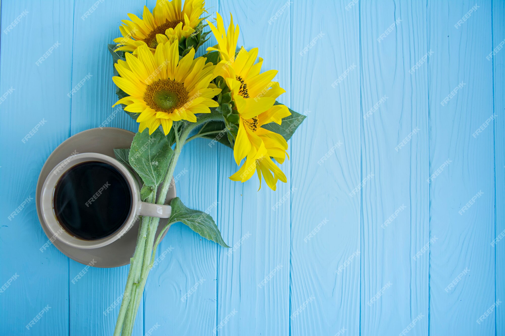 Una taza de café, granos de café, canela y girasol sobre un fondo azul.  humor de verano | Foto Premium