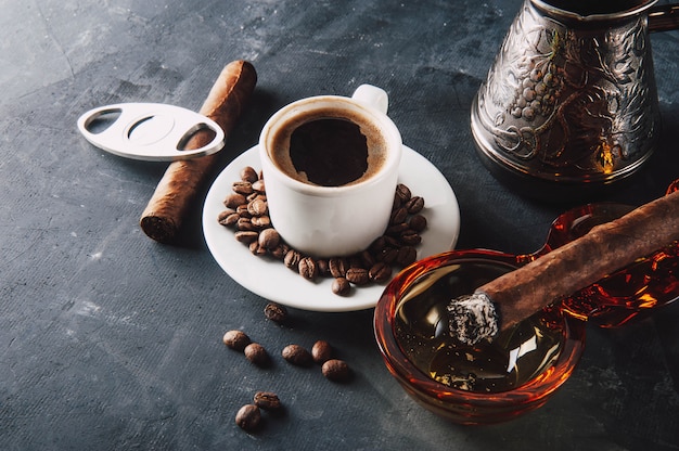 Taza de café, granos de café, cenicero con cigarro oscuro