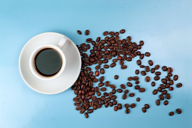 Taza de café y granos de café esparcidos en azul