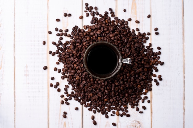 Taza de café y granos de café en la mesa de madera blanca