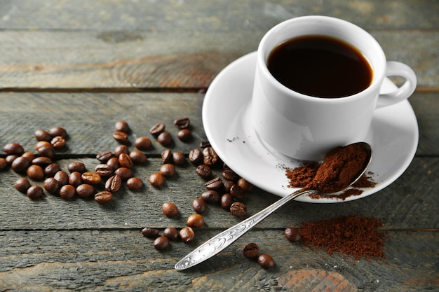 Taza de café y granos de café en la mesa de madera sobre fondo gris