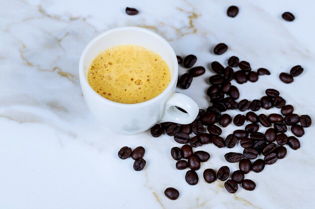 Taza de café y granos de café en la mesa de mármol