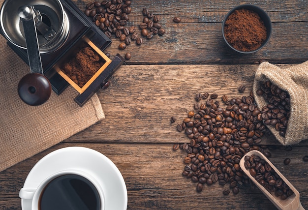 Una taza de café, granos de café y un molinillo de café en una pared de madera. Vista superior con espacio de copia.