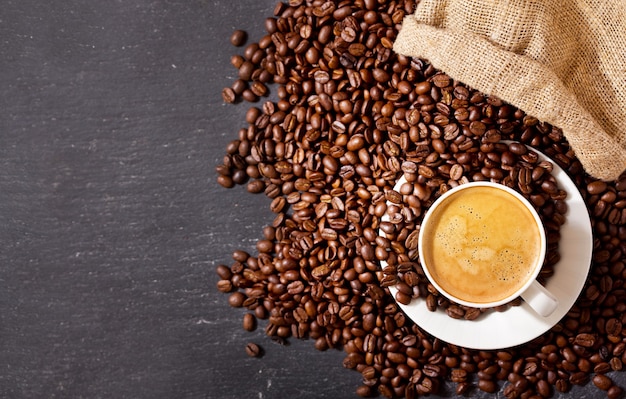 Foto taza de café y granos de café en un saco sobre fondo oscuro, vista superior