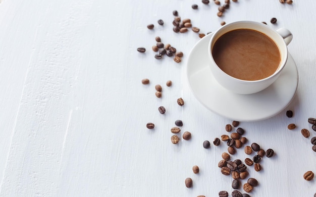 Taza de café y granos de café sobre fondo blanco de madera