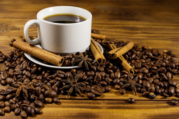 Taza de café, granos de café tostados, anís estrellado y palitos de canela en la mesa de madera