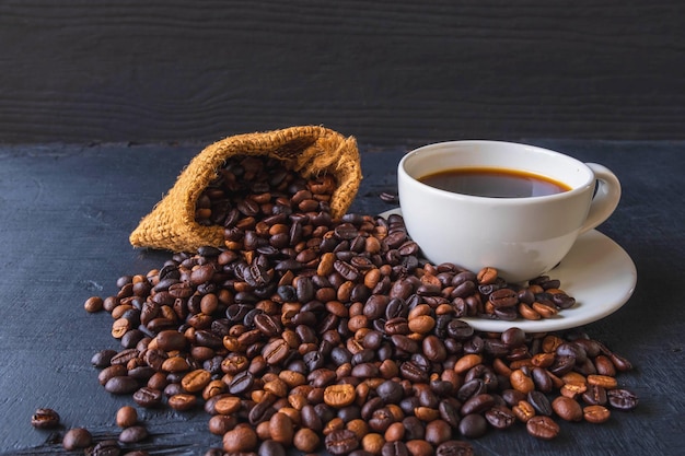 Una taza de café y granos de café tostados en una bolsa de saco marrón.