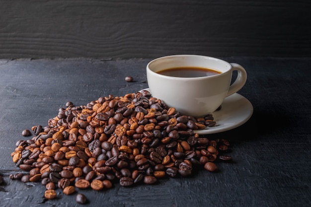 Taza de café y granos de café tostados sobre fondo negro