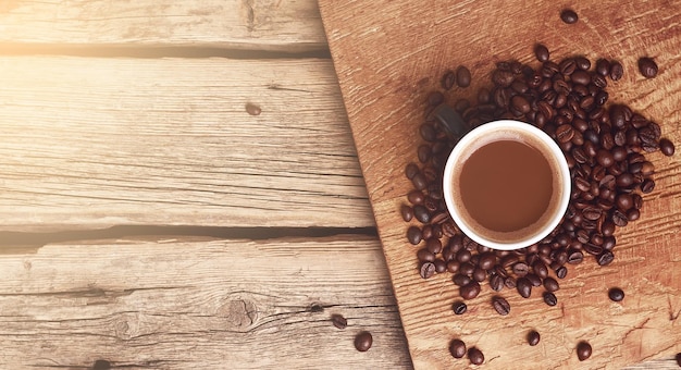 Taza de café y granos fritos en una mesa de madera con espacio para copiar