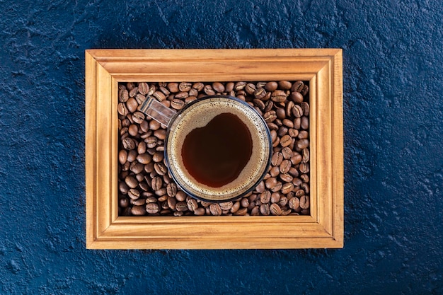 Taza de café y granos en un marco de madera sobre fondo azul.