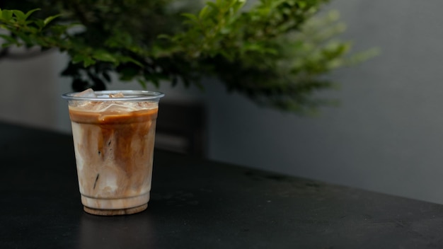 Una taza de café helado se sienta en una mesa frente a un árbol.