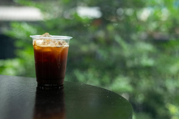 Una taza de café helado se sienta en una mesa frente a una ventana.