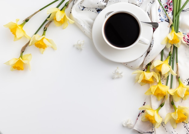 Taza de café con hermosas flores de narciso en la mesa blanca