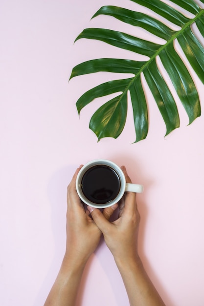 Taza de café y hoja de palma tropical en fondo rosado.