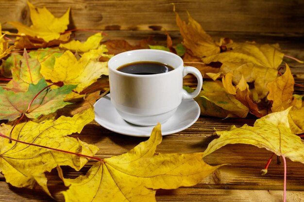 Taza de café y hojas de arce otoñales en la mesa de madera Concepto de otoño