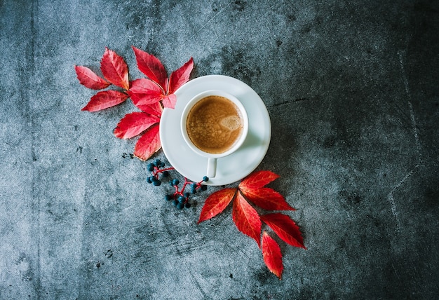 Taza de café con hojas de otoño rojas y bayas sobre un fondo de hormigón